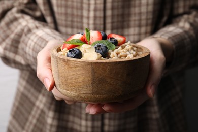 Photo of Woman holding bowl of tasty oatmeal with strawberries, blueberries and almond petals , closeup