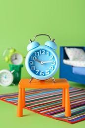 Photo of Light blue alarm clock as winner on stool near losing competitors against green background. Competition concept