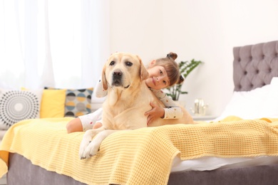 Photo of Adorable yellow labrador retriever and little girl on bed at home