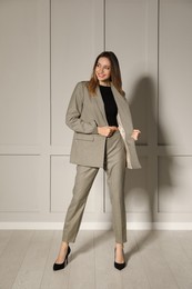Photo of Full length portrait of beautiful young woman in fashionable suit near light grey wall indoors. Business attire