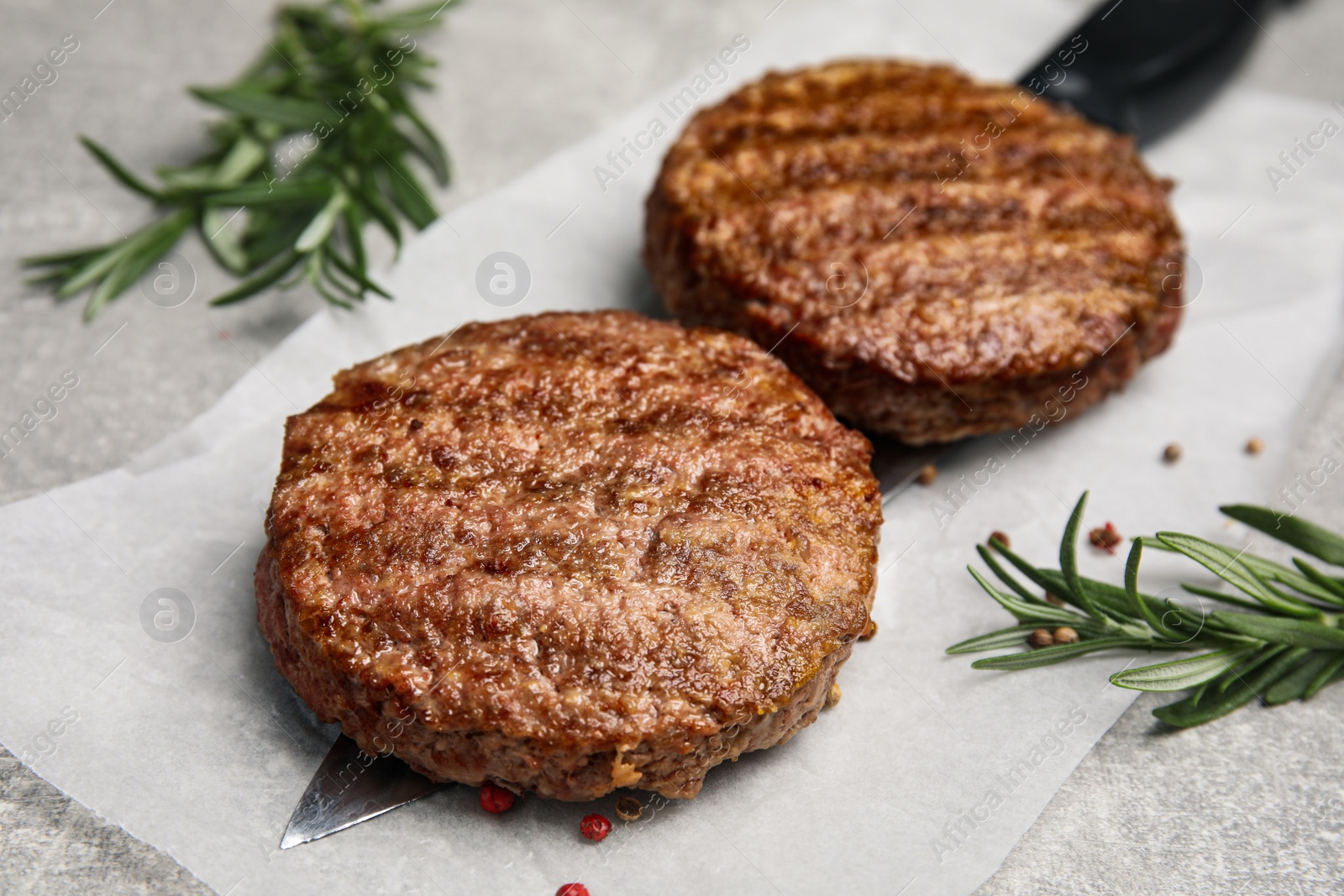 Photo of Tasty grilled hamburger patties, knife and seasonings on grey table, closeup