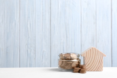 Photo of House model and jar with coins on table against wooden background. Space for text