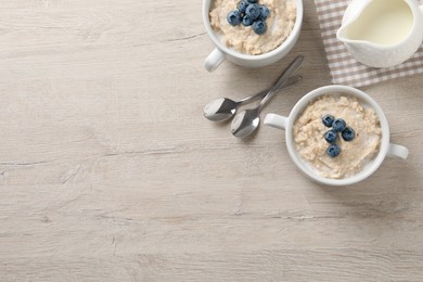 Photo of Tasty oatmeal porridge with blueberries served on light wooden table, flat lay. Space for text