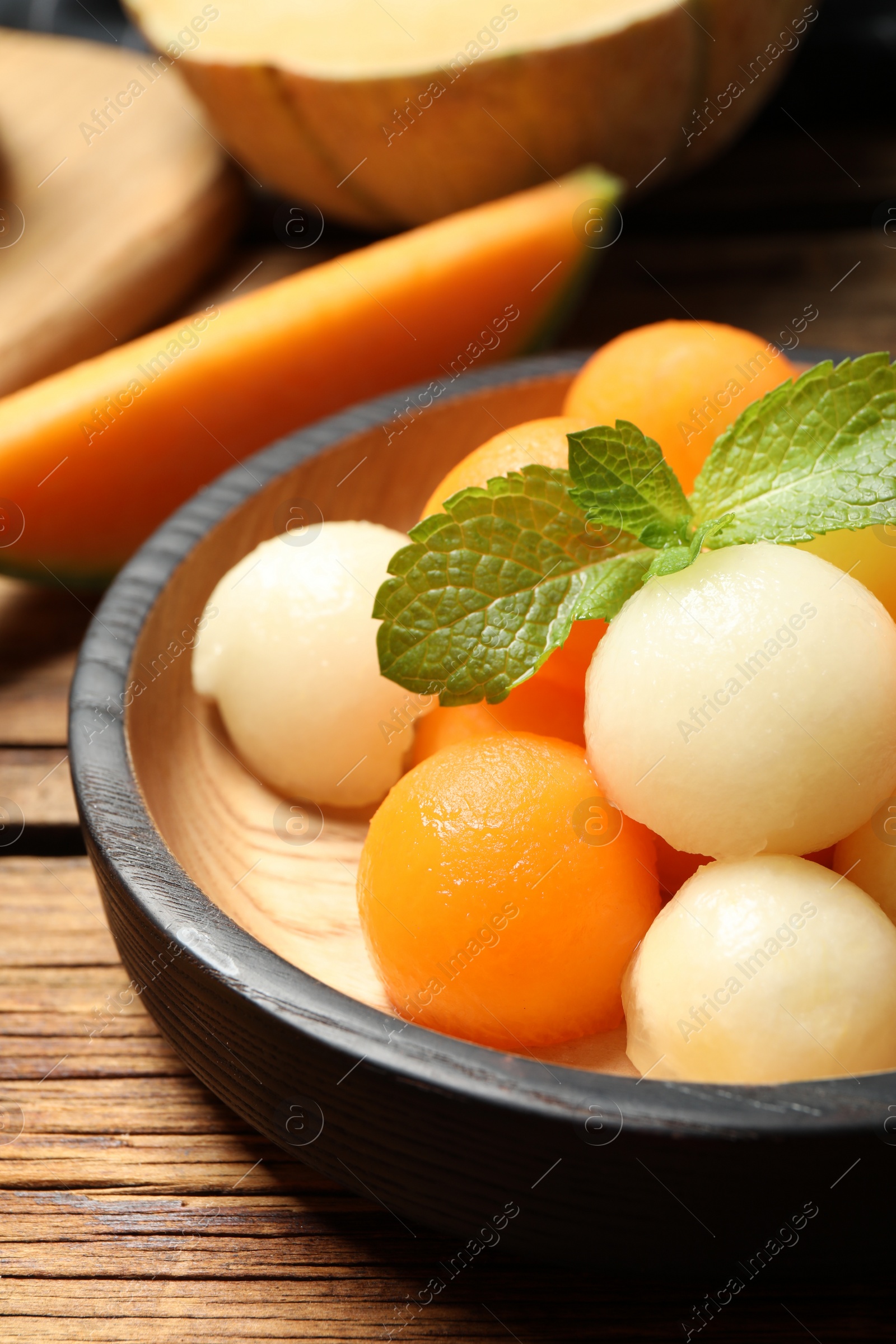 Photo of Different melon balls with mint on wooden table, closeup