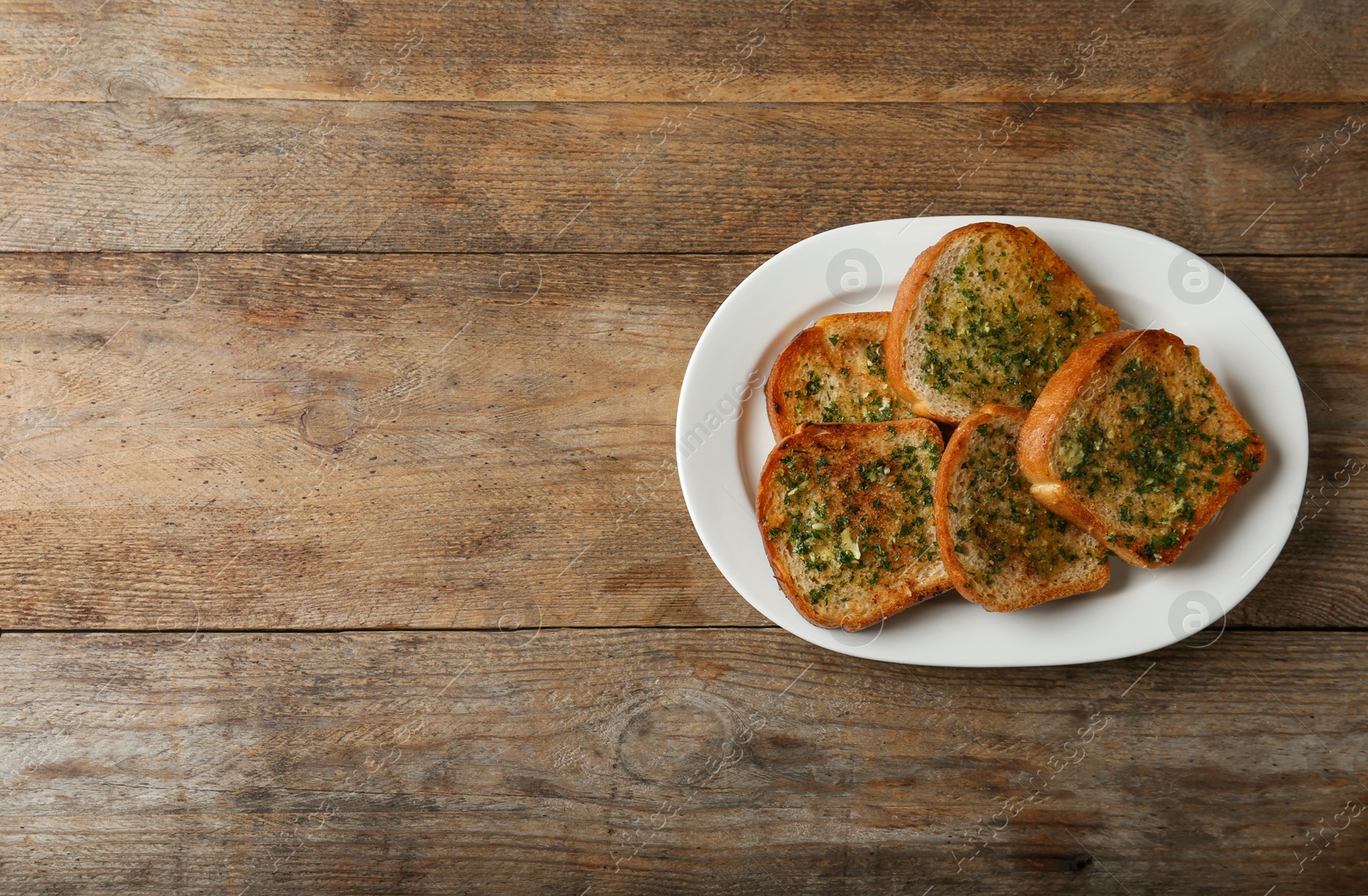 Photo of Slices of toasted bread with garlic and herbs on wooden table, top view. Space for text