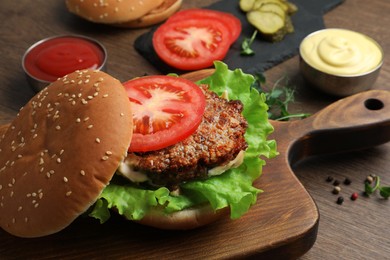 Photo of Delicious burger with beef patty and ingredients on wooden table, closeup