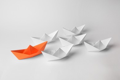 Photo of Group of paper boats following orange one on white background. Leadership concept