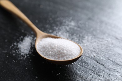 Photo of Organic white salt in spoon on black table, closeup. Space for text