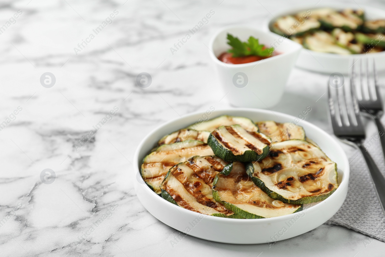 Photo of Grilled zucchini slices served on white marble table. Space for text