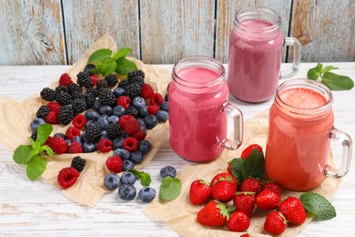 Photo of Mason jars of different berry smoothies and fresh ingredients on white wooden table, above view