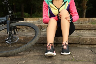 Photo of Woman with injured knee on steps near bicycle outdoors, closeup