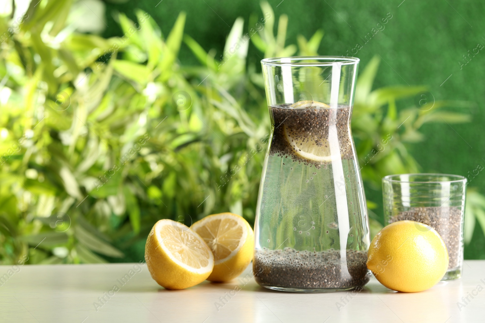 Photo of Glass and jug of lemon water with chia seeds on table. Space for text