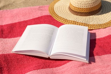 Photo of Open book, hat and striped towel on sandy beach