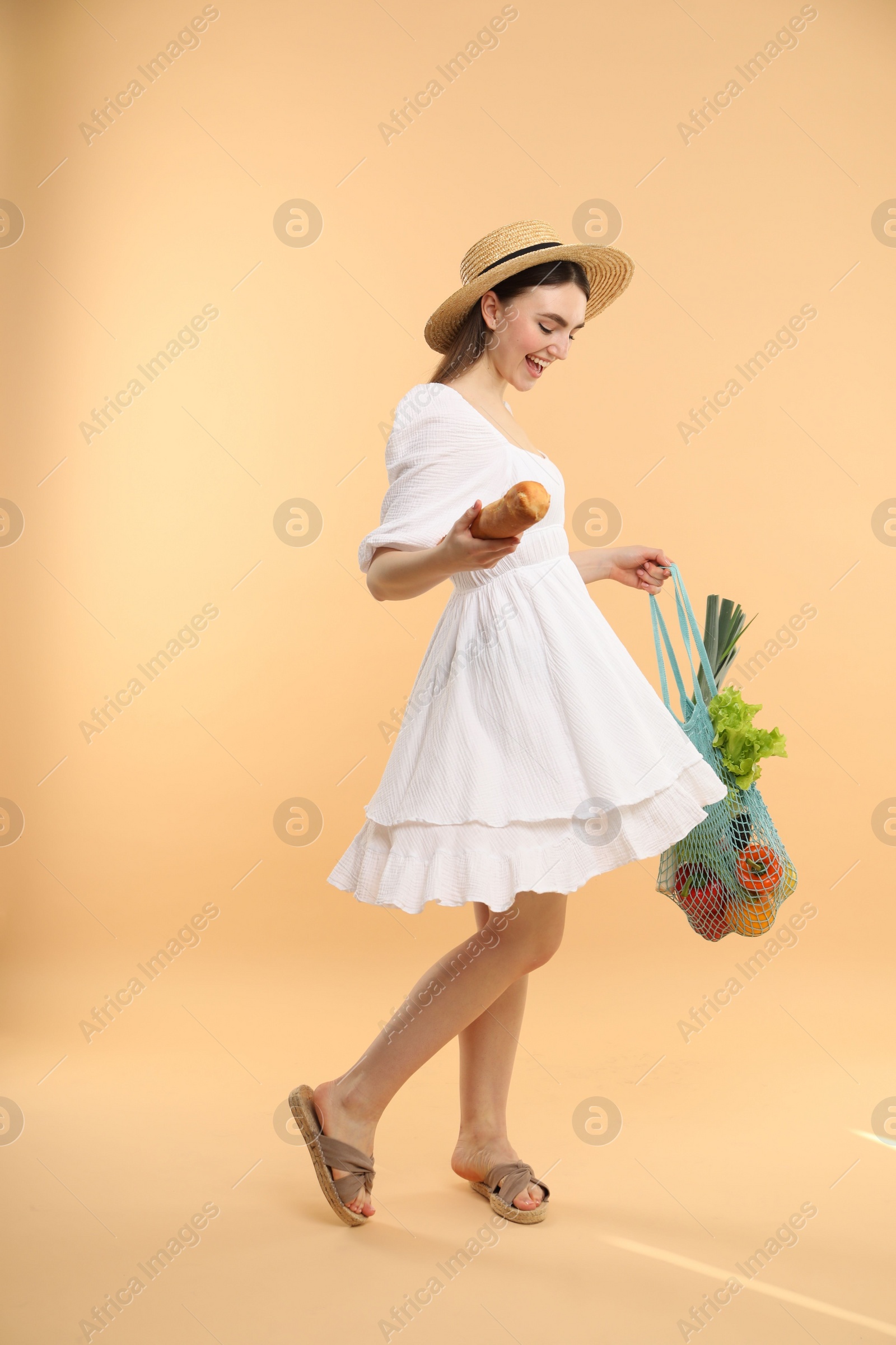 Photo of Woman with string bag of fresh vegetables and baguette on beige background