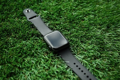 Photo of Modern stylish smart watch on green grass, closeup