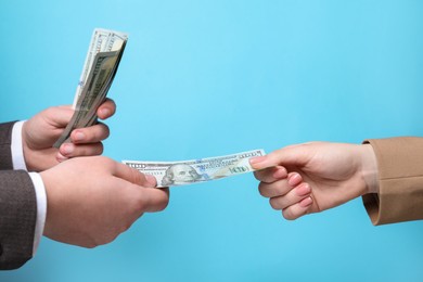 Photo of Man giving money to woman on light blue background, closeup. Currency exchange