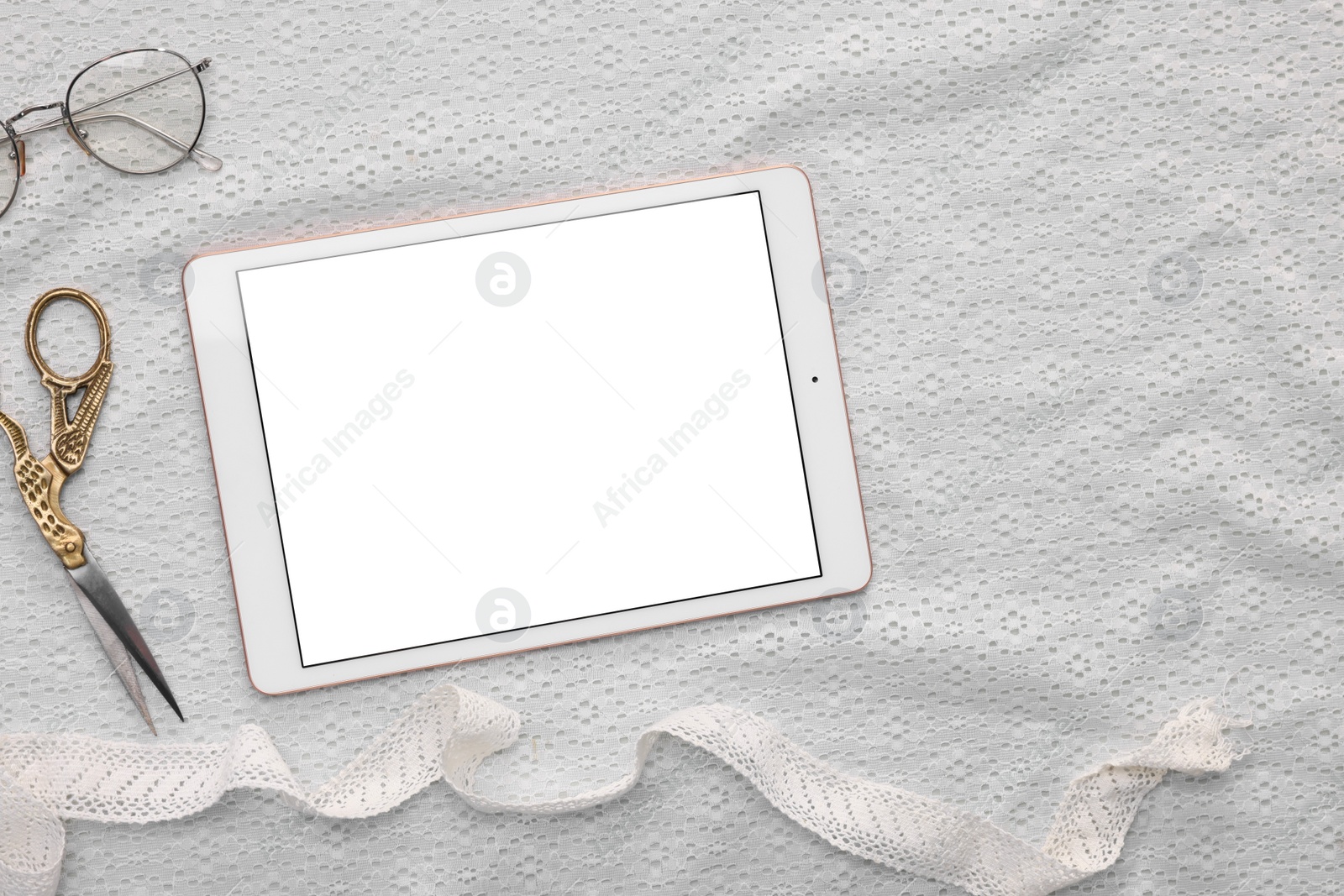 Photo of Modern tablet, glasses, scissors and ribbon on white fabric, flat lay. Space for text