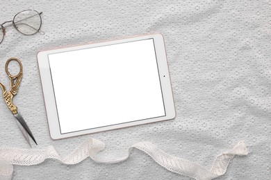 Modern tablet, glasses, scissors and ribbon on white fabric, flat lay. Space for text