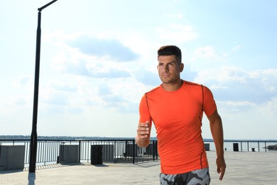 Photo of Handsome man in sportswear running outdoors on sunny day