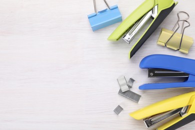 Photo of Bright staplers with staples and binder clips on light wooden table, flat lay. Space for text