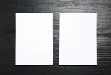Photo of Blank paper sheets for brochure on black wooden background, flat lay. Mock up