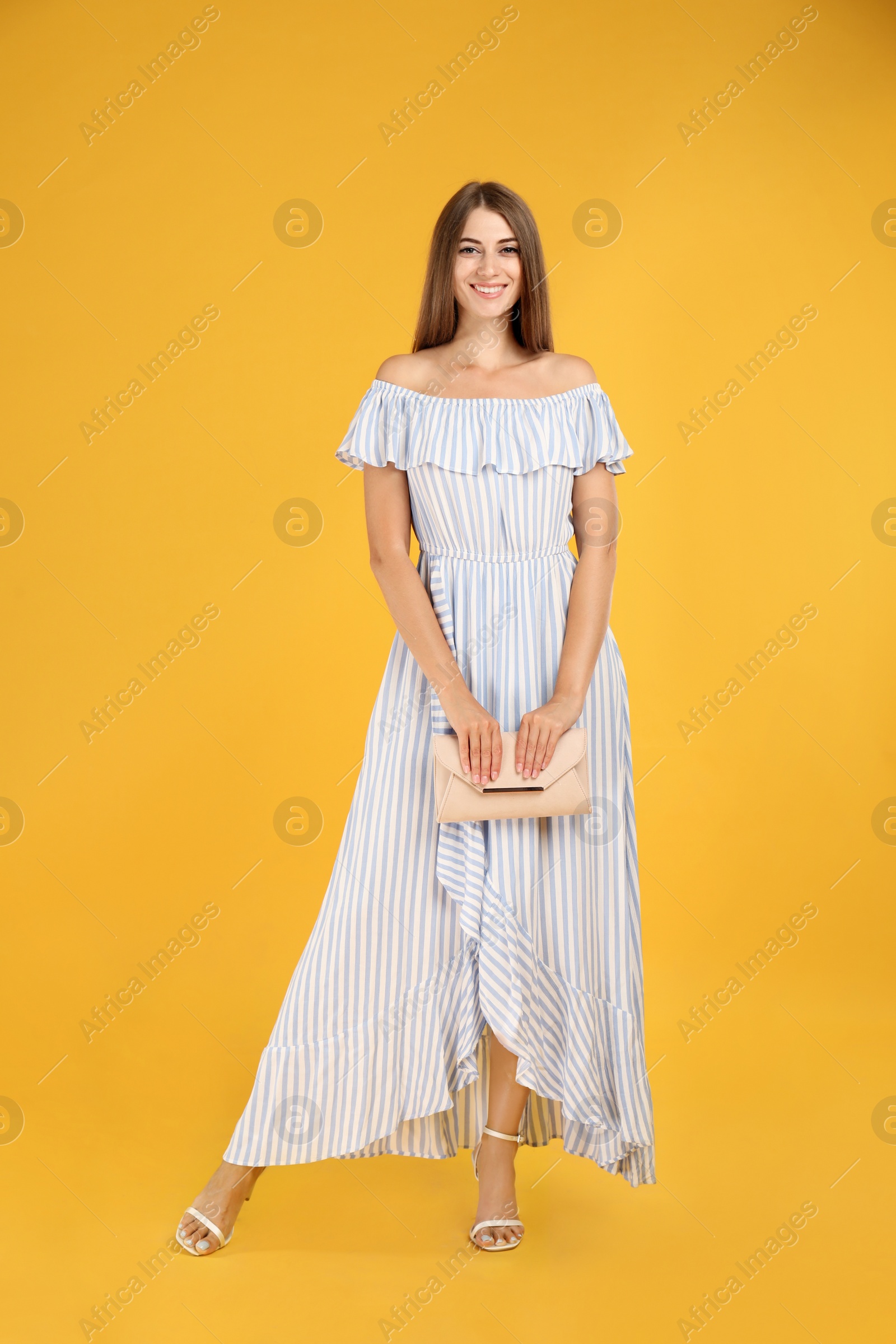 Photo of Young woman wearing stylish dress with elegant clutch on yellow background