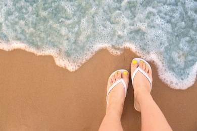 Photo of Top view of woman with white flip flops on sand near sea, space for text. Beach accessories