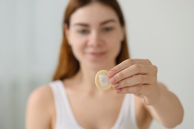 Photo of Woman holding condom indoors, selective focus. Safe sex
