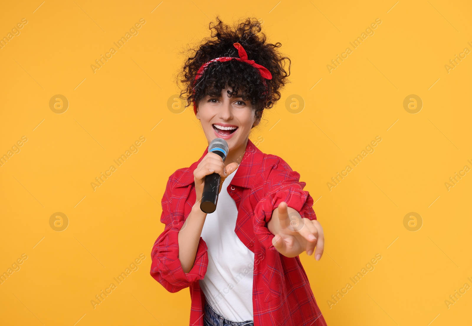 Photo of Beautiful young woman with microphone singing on yellow background