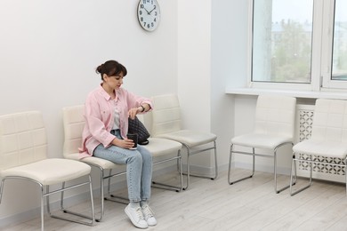 Woman with cup of drink looking at wrist watch and waiting for appointment indoors