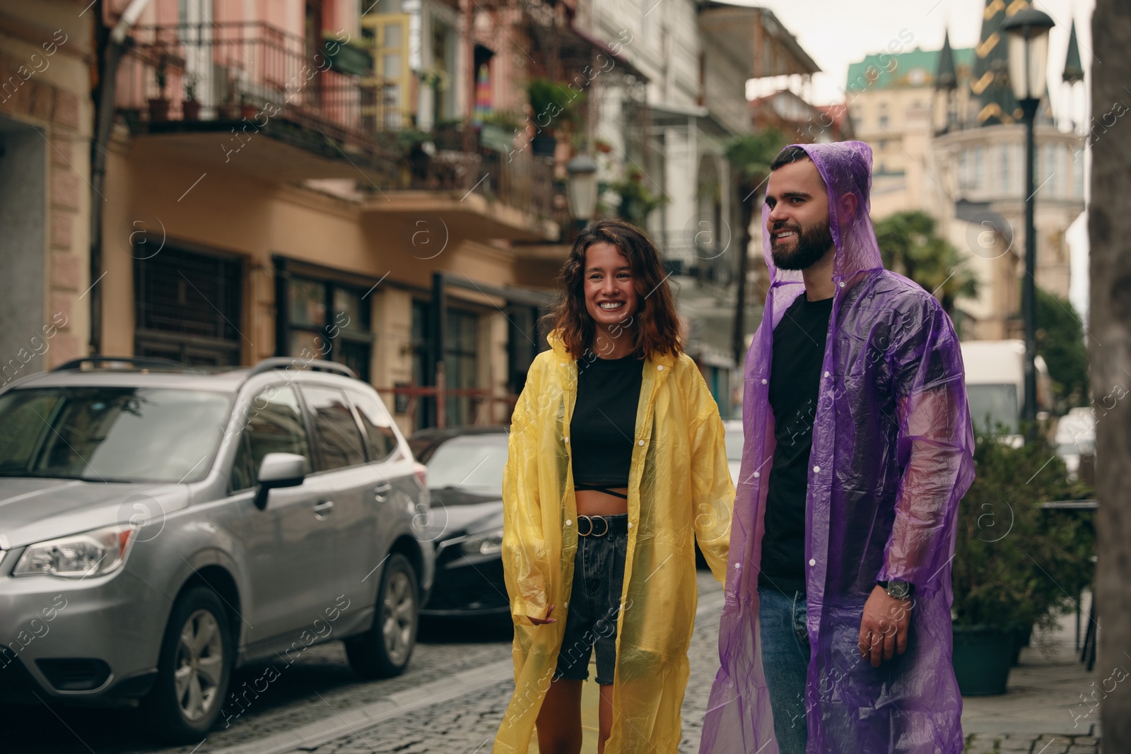 Photo of Young couple in raincoats enjoying time together on city street, space for text