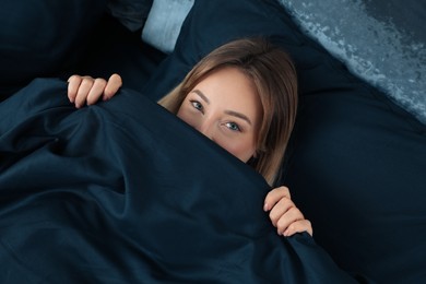 Photo of Young woman in comfortable bed with dark blue linens, above view