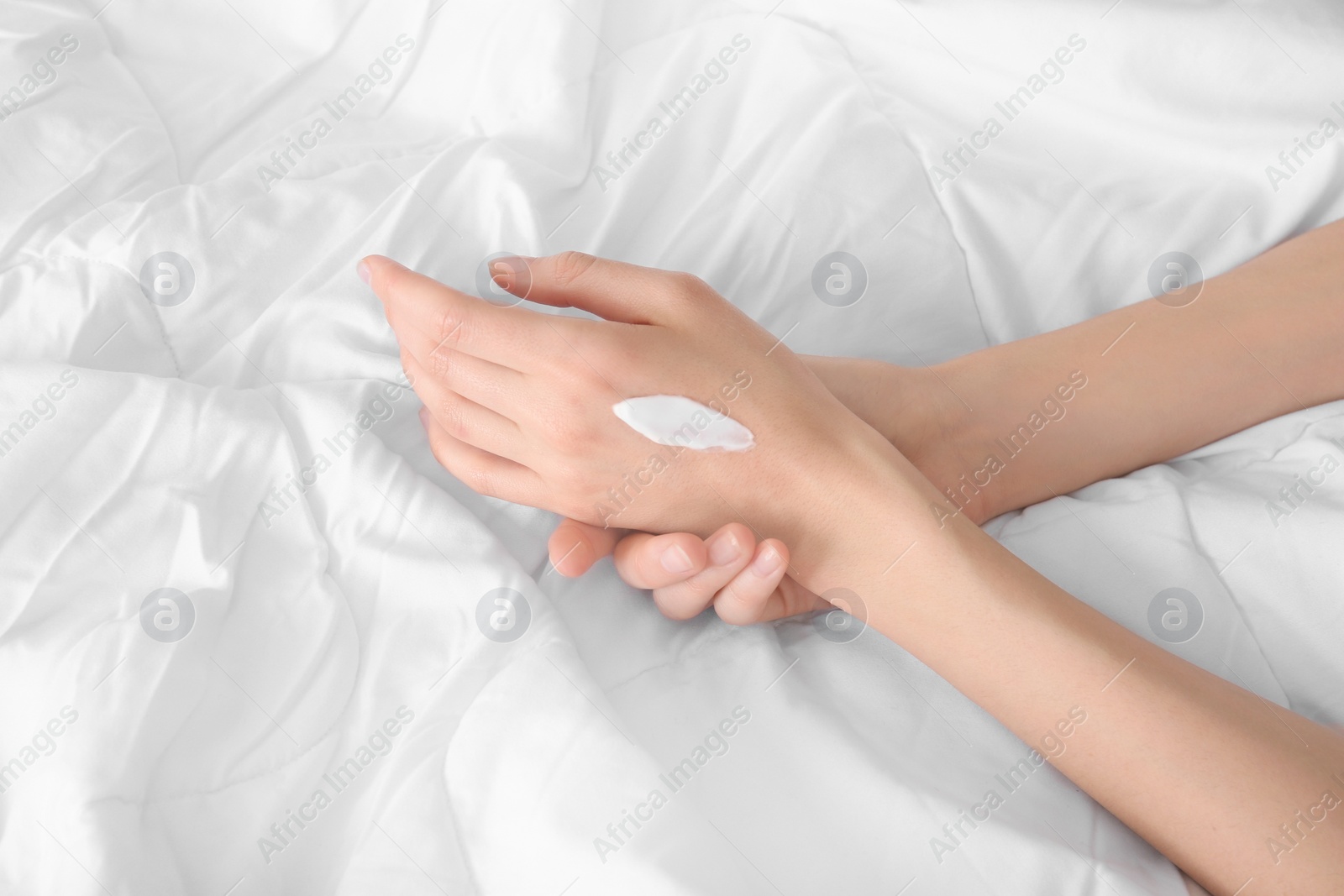 Photo of Young woman applying cream onto hands, indoors