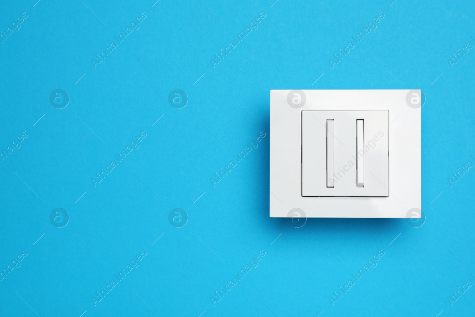 Photo of White light switch on light blue background, top view. Space for text