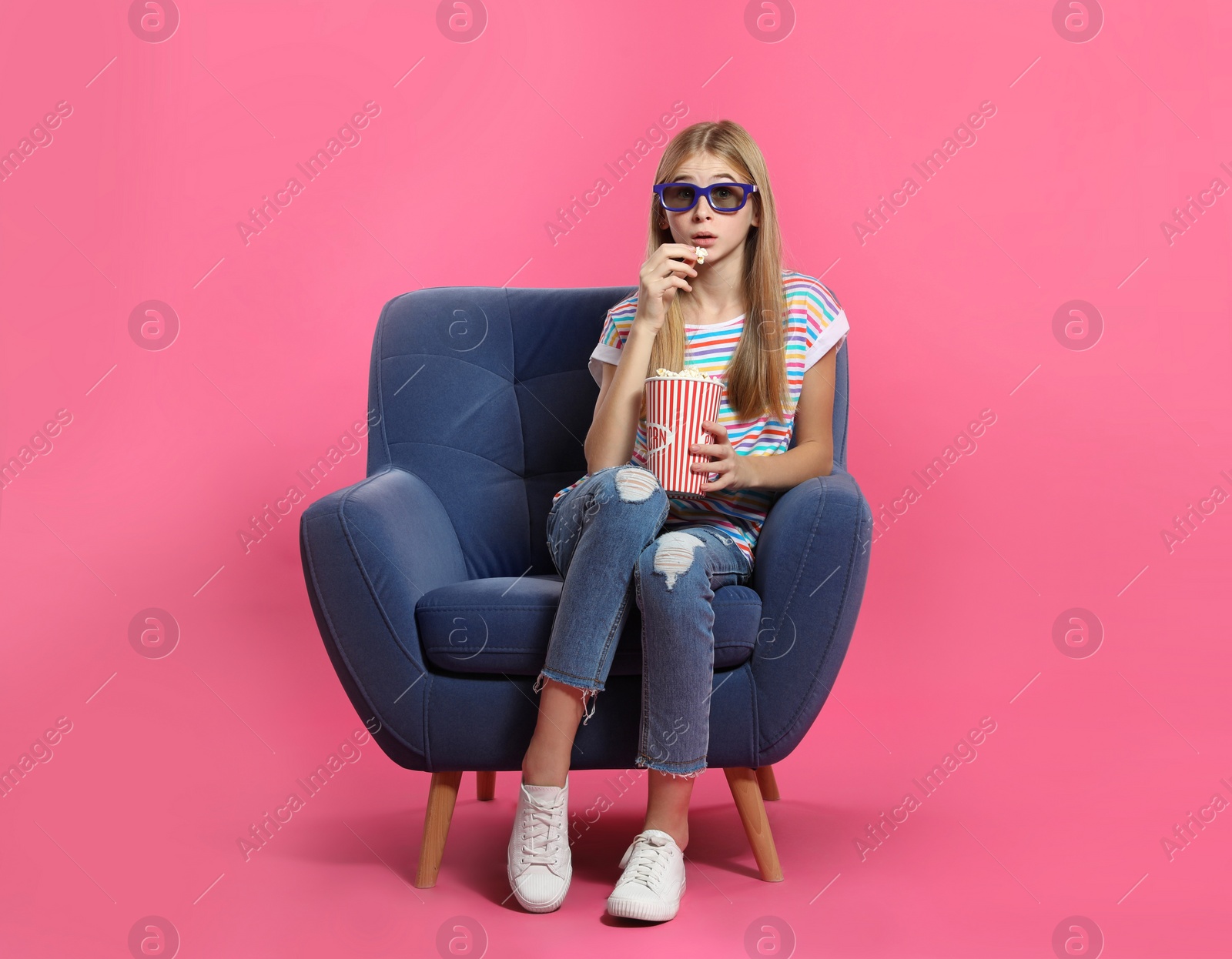 Photo of Emotional teenage girl with 3D glasses and popcorn sitting in armchair during cinema show on color background