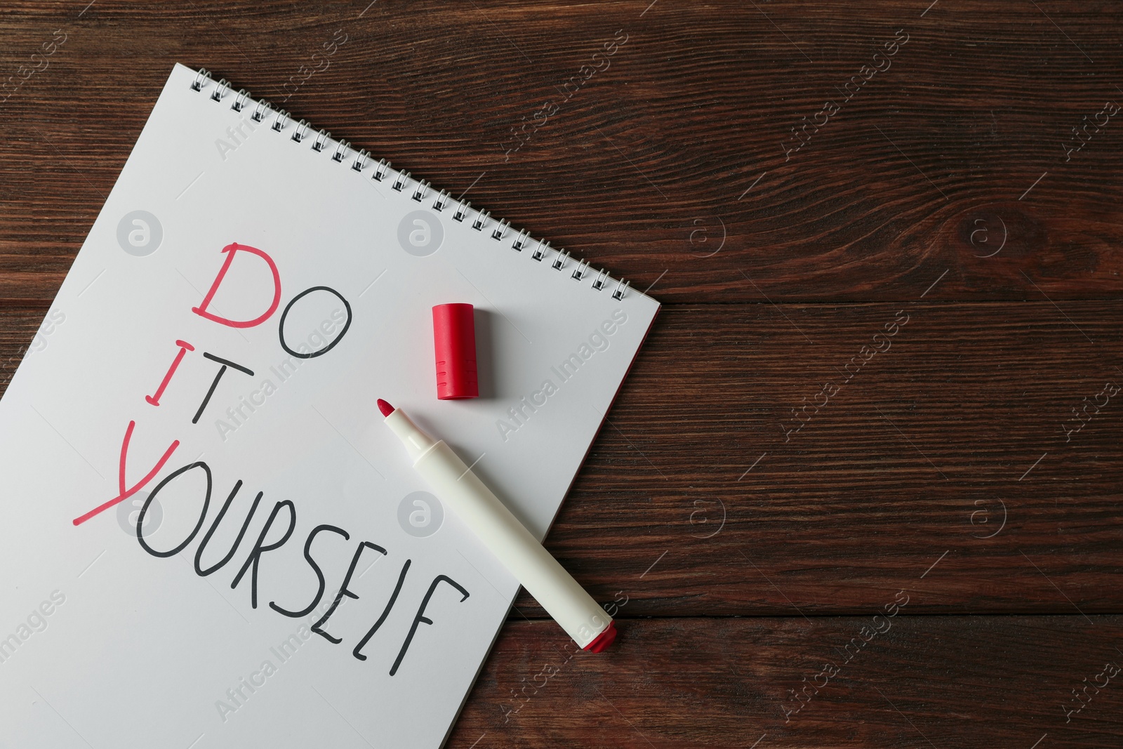 Photo of Notebook with phrase Do It Yourself and marker on wooden table, flat lay with space for text. DIY concept