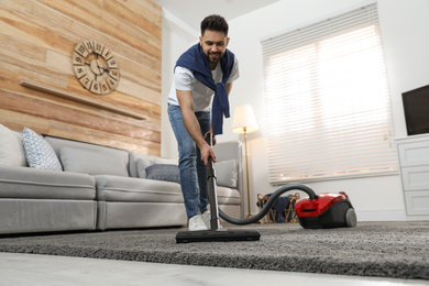 Photo of Young man using vacuum cleaner at home