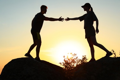 Hiker helping friend outdoors at sunset. Help and support concept