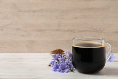 Glass cup of delicious chicory drink and flowers on white wooden table, space for text