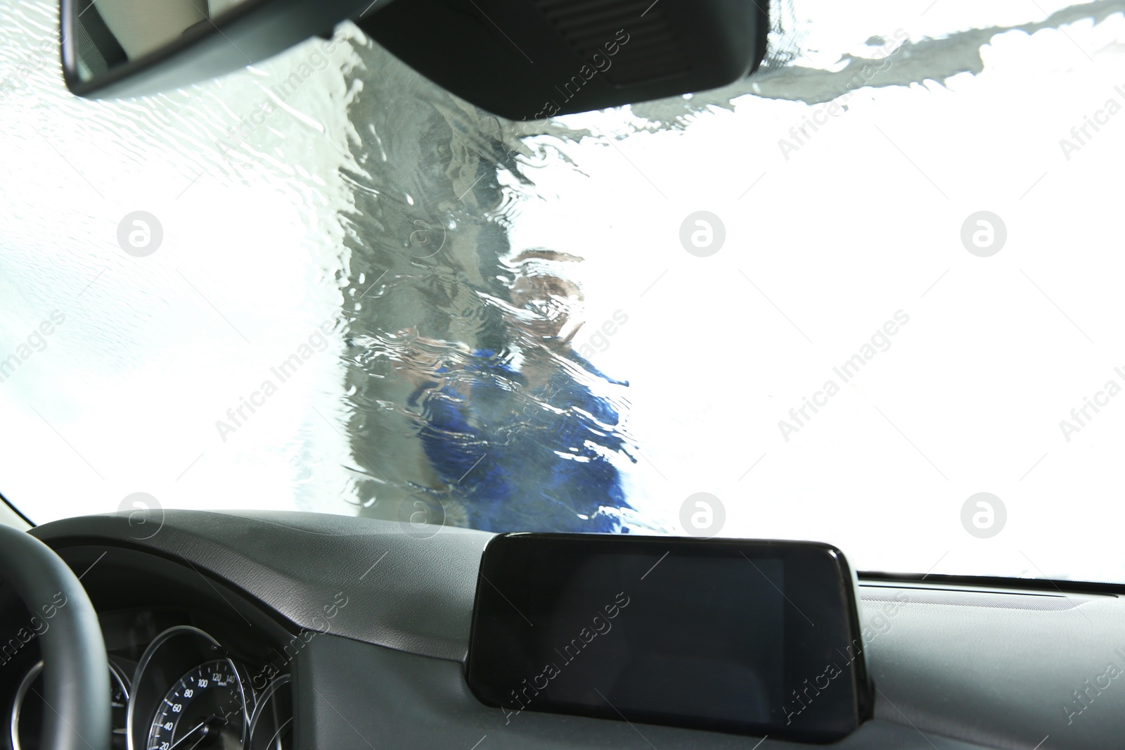 Photo of Worker cleaning automobile windshield with high pressure water jet at car wash, view from inside