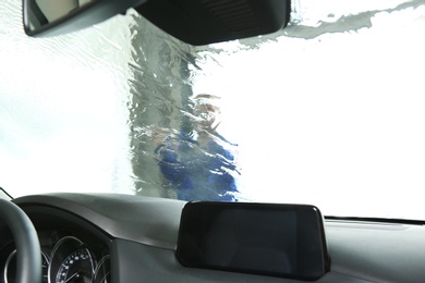 Photo of Worker cleaning automobile windshield with high pressure water jet at car wash, view from inside