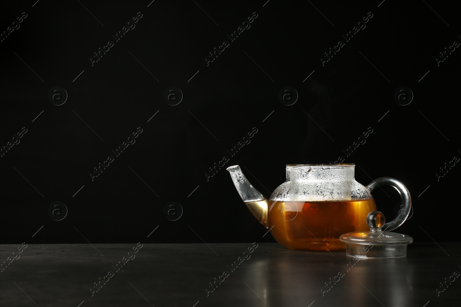 Photo of Glass teapot with delicious hot beverage on table against dark background. Space for text