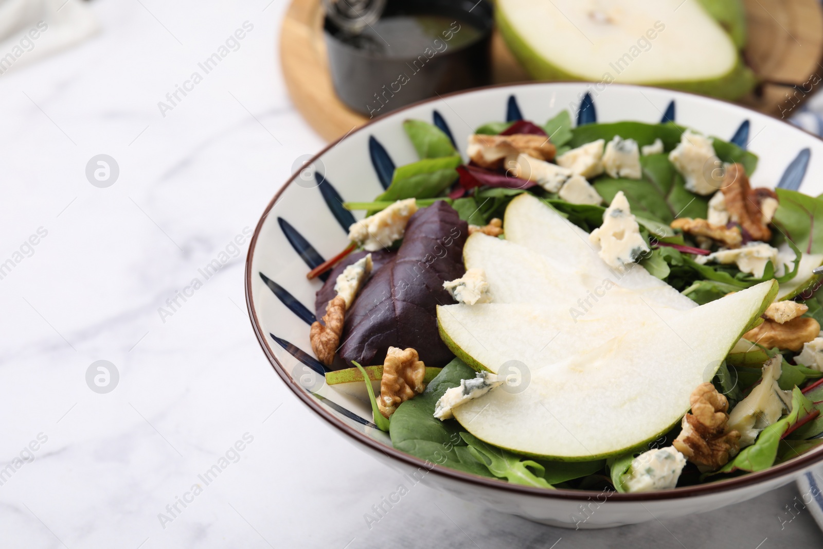 Photo of Delicious pear salad in bowl on white marble table, closeup. Space for text