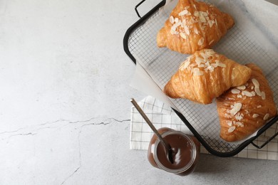 Photo of Delicious croissants with almond flakes and chocolate paste on light grey table, flat lay. Space for text