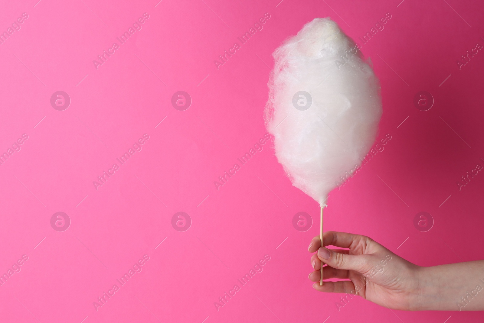 Photo of Woman holding sweet cotton candy on pink background, closeup. Space for text