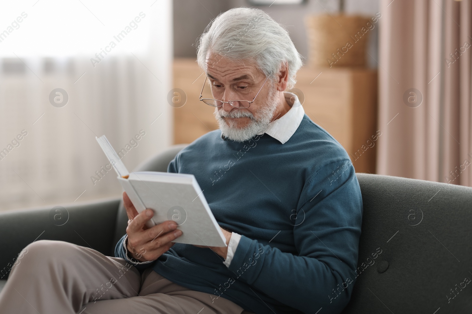 Photo of Portrait of happy grandpa reading book on sofa indoors