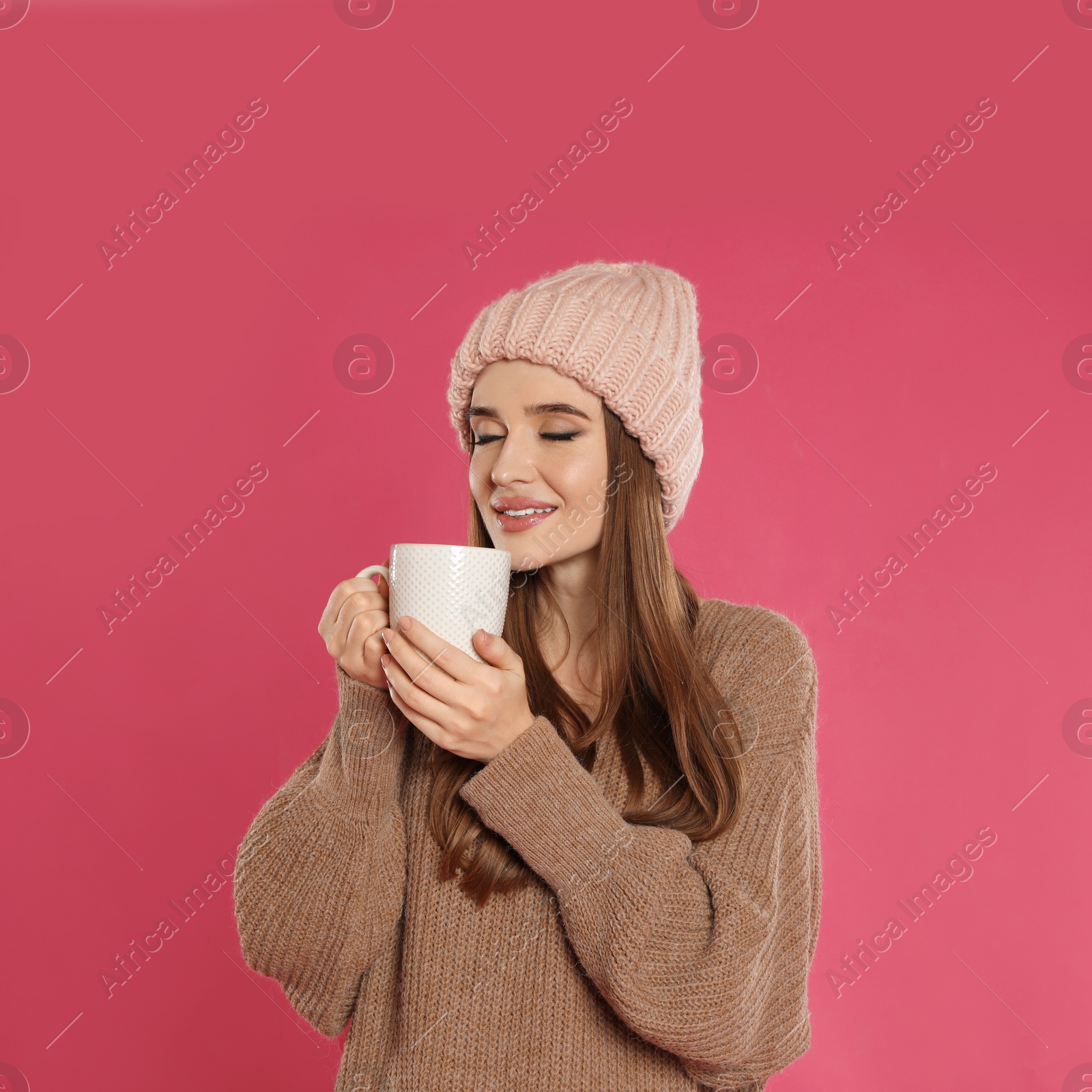 Photo of Beautiful young woman in hat and sweater with drink on pink background. Winter season