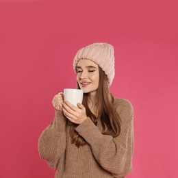 Photo of Beautiful young woman in hat and sweater with drink on pink background. Winter season