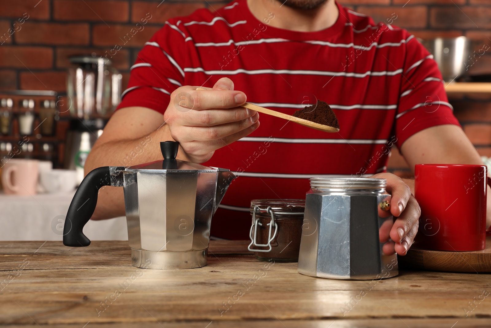 Photo of Man putting ground coffee into moka pot at wooden table in kitchen, closeup