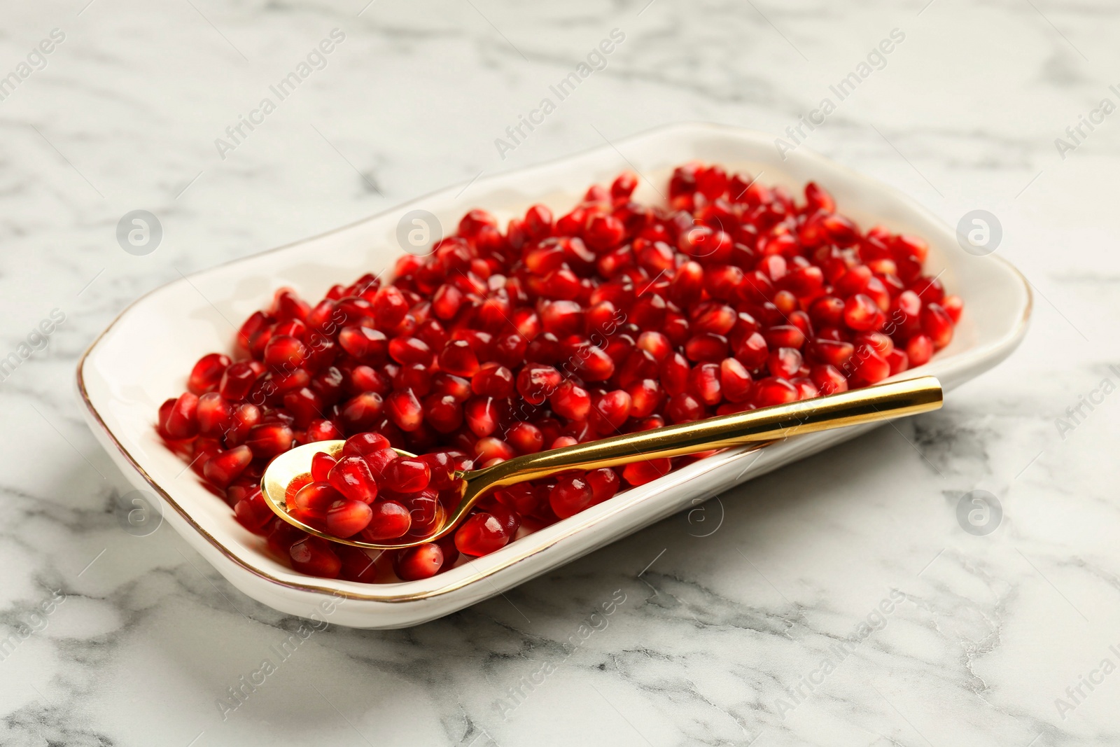 Photo of Ripe juicy pomegranate grains on white marble table